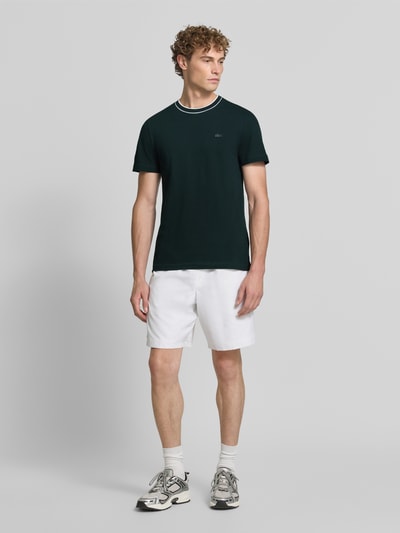 Męski model nosi Regular Fit T-Shirt aus Baumwoll-Mix von Lacoste w kolorze ciemnej zieleni na białym tle, całkowity widok z przodu