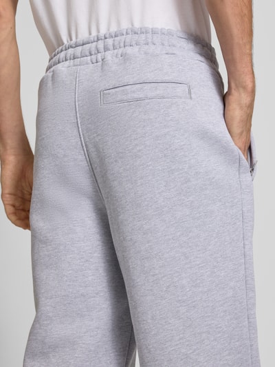 Männermodel trägt Loose Fit Sweatpants aus Baumwoll-Mix mit Label-Detail von PEGADOR in Hellgrau, sichtbare Eingrifftaschen, Detailaufnahme Rückansicht. Innenbeinlänge bei Größe M: 70 cm, elastischer Bund