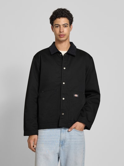 Männermodel trägt schwarze Jacke mit Umlegekragen und Label-Detail von Dickies, Material-Mix mit Baumwoll-Anteil, Regular-Fit, Knopfleiste, Eingrifftaschen, Rückenlänge 75 cm, Schulterbreite 47 cm, Brustweite 64 cm, Ärmellänge 66 cm, Ganzkörperansicht von vorne.