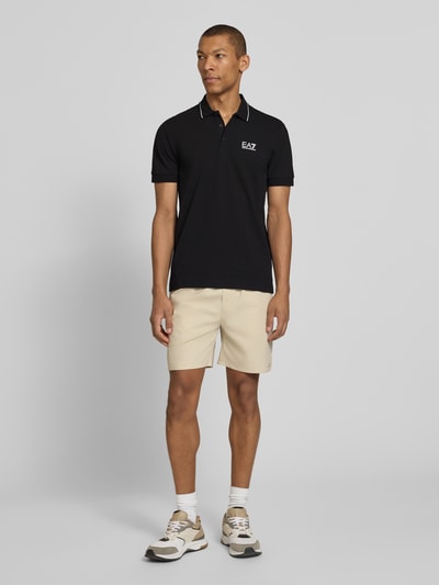 Männermodel trägt Regular Fit Poloshirt mit Logo-Print von EA7 Emporio Armani, Schwarz, Baumwoll-Mix, Kurzarm, Ganzkörperansicht von vorne.