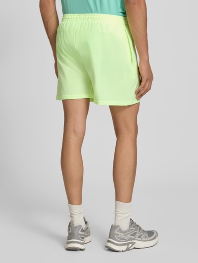 Männermodel trägt Shorts mit elastischem Bund und Logo von New Balance, Regular-Fit, neongrün, glatte Struktur, Ganzkörperansicht Rückansicht.
