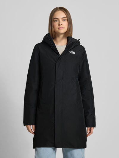 Vrouwenmodel draagt lange jas met capuchon Model 'SUZANNE' van The North Face, Recht pasvorm, labeldetail, zwarte effen kleur, steekzakken, ritssluiting, ruglengte maat S 92 cm, schouderbreedte 40 cm, borstwijdte 48 cm, mouwlengte 66 cm, geheel vooraanzicht