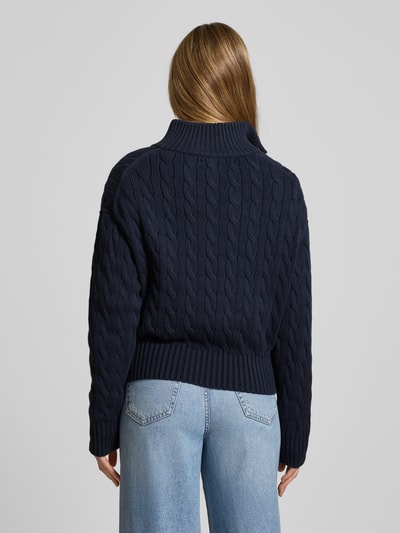 Vrouwenmodel draagt Troyer met kabelpatroon van Polo Ralph Lauren van puur katoen, regular fit, opstaande kraag met ritssluiting, logostitching, elastische boorden, kleur donkerblauw, gebreide structuur, ruglengte maat S 53 cm, mouwlengte 55 cm. Ganzkörperansicht Rückansicht.