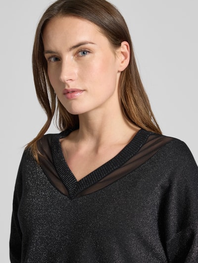 Kobiece modelka nosi Relaxed Fit Pullover aus Viskose-Mix in Strick-Optik od LIU JO SPORT, półprzezroczyste partie, czarny kolor, długi rękaw, dekolt V, luźny krój, elastyczne wykończenia, widoczna struktura dzianiny, kontekst: damski pulower Relaxed Fit z wiskozy, długość tyłu 59 cm, długość rękawa 49 cm, zbliżenie górnej części ciała.