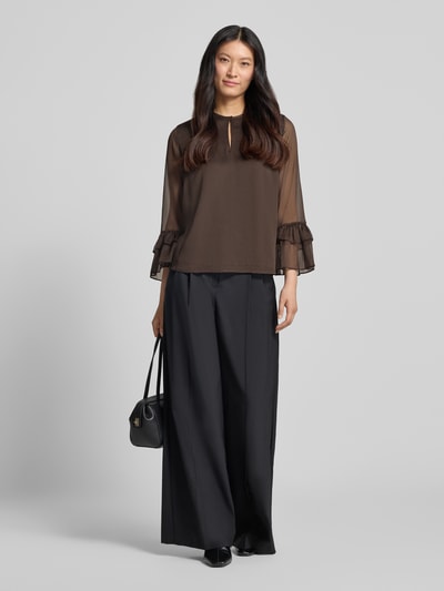 Vrouwenmodel draagt Bluse mit Volant-Ärmeln van comma, bruin met transparante Volantmouwen, zwarte wijde broek, los model, ronde hals met knoopsluiting, lang mouwen, ruglengte maat 36: 62 cm, mouwlengte maat 36: 55 cm, Ganzkörperansicht von vorne.