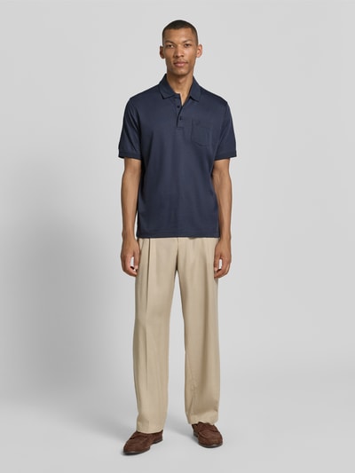 Männermodel trägt Regular Fit Poloshirt mit Brusttasche und Label-Stitching von bugatti in Dunkelblau, Polokragen, Knopfleiste, Rückenlänge bei Größe M 70 cm, Ganzkörperansicht von vorne.