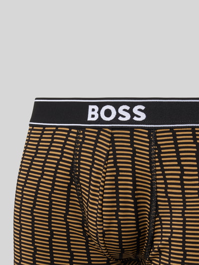 Mężczyzna nosi obcisłe bokserki z mieszanki bawełny od BOSS, wzór w żółto-czarne paski, zbliżenie na pas z logo.