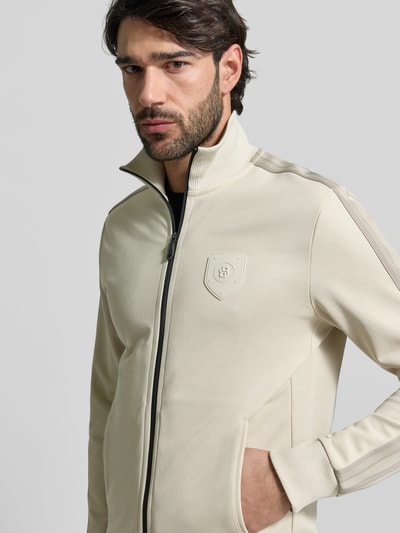 Männermodel trägt Regular Fit Sweatjacke mit Baumwoll-Anteil Modell 'LUX SKARLEY' von BOSS Green in Beige, Galonstreifen, Label Patch, Nahaufnahme Oberkörper.