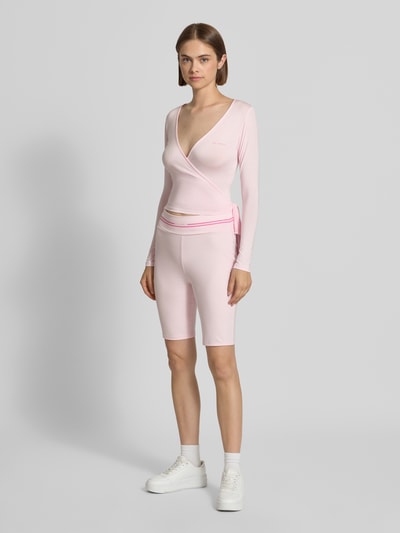 Frauenmodel trägt Cardigan in Wickel-Optik Modell 'Luca' von OH APRIL in zartem Rosa, feine Struktur, V-Ausschnitt, Ganzkörperansicht von vorne. Modal-Elasthan-Mix, Slim Fit, Rückenlänge Größe S 46 cm.