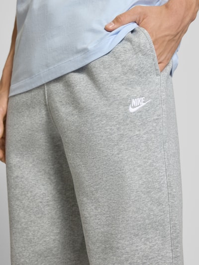 Männermodel trägt graue Sweatpants mit Logo-Stitching und Eingrifftaschen von Nike, Baumwoll-Mix, Nahaufnahme Oberschenkel.