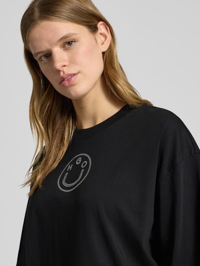 Modelka nosi czarny damski t-shirt Oversized T-Shirt aus reiner Baumwolle Modell 'Oversized_Tee_b_9' od HUGO, efekt: jednolity kolor, krój oversized fit, błyszczący nadruk, okrągły dekolt, krótki rękaw, wykończenie: proste, wykończenie materiału: dżersej, materiał: bawełna, zbliżenie górnej części ciała.