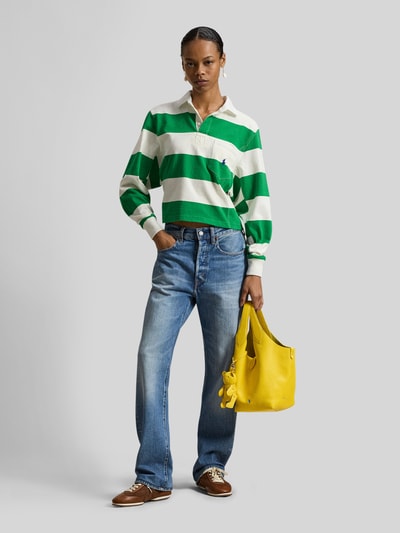 Modelka nosi Regular Fit Poloshirt aus reiner Baumwolle od Polo Ralph Lauren, piqué, w zielono-białe szerokie pasy, logo, długi rękaw, kołnierzyk polo, trzy guziki, elastyczne mankiety, kieszonka na piersi, widok całej sylwetki z przodu.