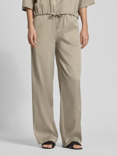 Frauenmodel trägt Wide Fit Stoffhose mit elastischem Bund Modell 'Consider' von Drykorn, sandfarben, lockerer Fall, Nahaufnahme Unterkörper. Cupro-Mix mit Baumwoll-Anteil, Gesäßtaschen, Bundweite 36 cm, Innenbeinlänge 84 cm.
