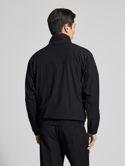 Mannelijk model draagt Regular Fit Trainingsanzug mit Label-Detail Modell LW_PS Spirit70 TT - PORSCHE X BOSS van BOSS Green in effen kleuren, opstaande kraag, lange mouwen, elastische rompzoom en pijpboord, tweedelig, piqué, labelopschrift, label in reliëf, ganzkörperaanzicht achteraan.