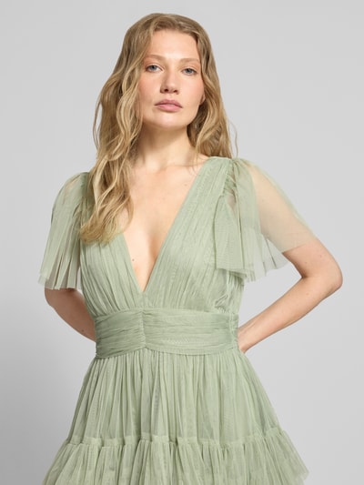 Frauenmodel trägt Cocktailkleid mit tiefem V-Ausschnitt von LACE & BEADS aus mintgrünem Tüll, Taillenband, Stufen-Look, Nahaufnahme Oberkörper.
