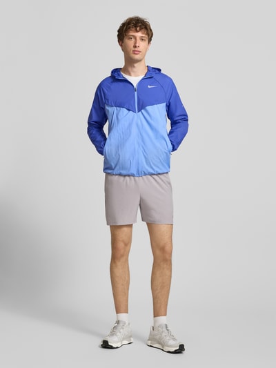 Männermodel trägt Trainingsjacke mit Logo-Print und Kapuze von NIKE TRAINING in zwei Blautönen, Reißverschluss, gerader Schnitt, Ganzkörperansicht von vorne.
