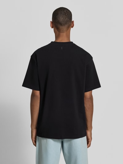 Männermodel trägt schwarzes Relaxed Fit T-Shirt aus reiner Baumwolle Modell 'MAARKOS' von ARMEDANGELS, glatte Struktur, Ganzkörperansicht Rückansicht.