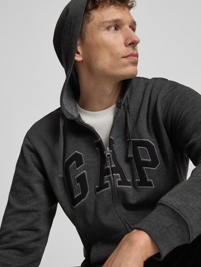 Männermodel trägt Sweatjacke mit Logo und Känguru-Tasche von GAP aus Baumwoll-Mix, Regular-Fit, Kapuze, Reißverschluss, Nahaufnahme Oberkörper.