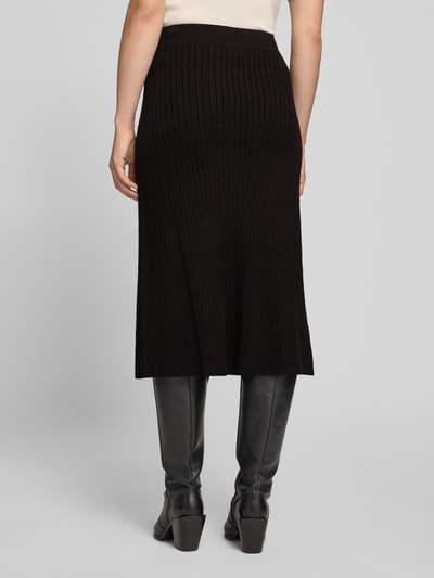 Frauenmodel trägt Strickrock aus Viskose-Mix mit Zopfmuster von Apricot, schwarz, gerader Schnitt, Midirock, elastischer Bund, Ganzkörperansicht Rückansicht.