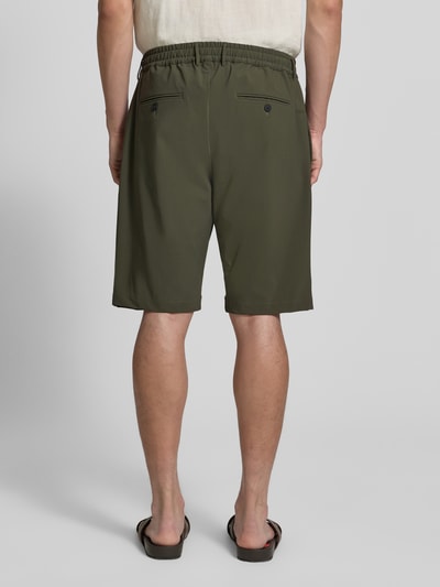Mężczyzna nosi Straight Fit Shorts mit elastischem Bund von CRUNA, oliwkowy kolor, kieszonki z tyłu, krój straight fit, szerokość w rozmiarze 50: 42 cm, długość nogawki od wewnątrz: 26 cm, widok całej sylwetki z tyłu.
