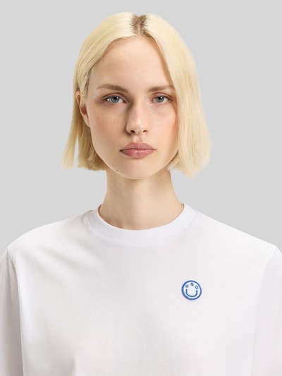 Frauenmodel trägt Relaxed Fit T-Shirt aus reiner Baumwolle Modell 'VINTAGE TEE_B_1' von Hugo Blue in Weiß mit Label Patch und Rundhalsausschnitt, Nahaufnahme Oberkörper.