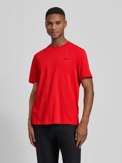 Męski model nosi Regular Fit T-Shirt aus reiner Baumwolle Modell 'DERO222' von HUGO, kolor czerwony, krój regular fit, nadruk z logo, okrągły dekolt, krótkie rękawy, materiał jersey. Ganzkörperansicht von vorne.