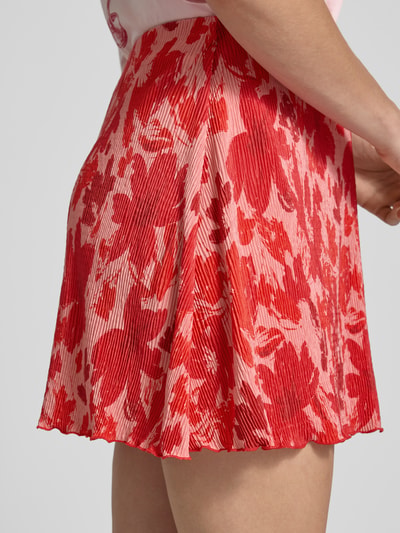Vrouwenmodel draagt Ausgestellter Mini-Rock met all-over motief model 'FLORA' van Pieces in rood en roze, dames rok, detailopname rechterzijaanzicht.