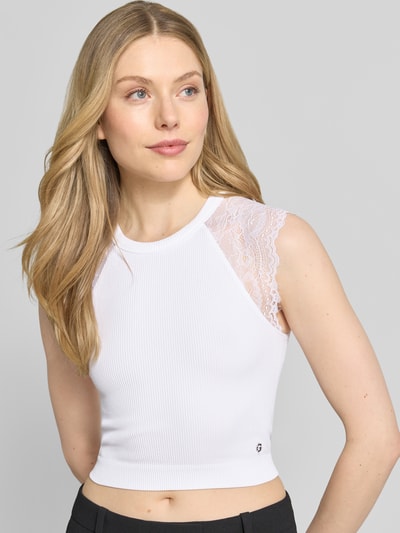 Kobiece modelka nosi Crop Top mit Spitzenbesatz Modell 'MILLIE' od Guess, biały materiał z domieszką stretchu, krój slim fit, cropped, koronka, damski top, długość tyłu w rozmiarze S: 37 cm, zdjęcie całego górnego tułowia z przodu