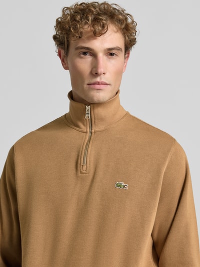 Männermodel trägt Regular Fit Troyer aus reiner Baumwolle von Lacoste in Hellbraun mit Reißverschluss und strukturierter Textur, Nahaufnahme Oberkörper. Herren Troyer von Lacoste.