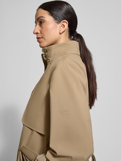 Frauenmodel trägt Regular Fit Mantel mit Stehkragen Modell 'Suva' von Rains, taillierte Passform, Stoffband, beige, Nahaufnahme Oberkörper.