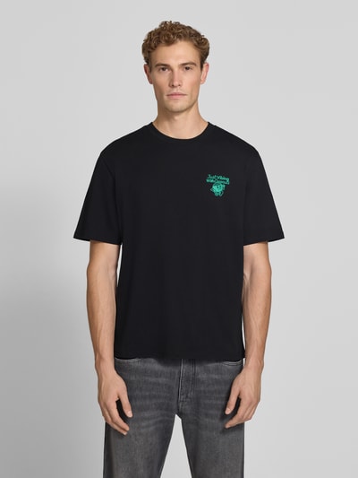 Männermodel trägt Regular Fit T-Shirt aus reiner Baumwolle Modell 'VIBING COCO' von REVIEW, Schwarz mit kleinem Print, Ganzkörperansicht von vorne, Herren T-Shirt von REVIEW x ANSON´S, Rückenlänge bei Größe M: 68 cm.