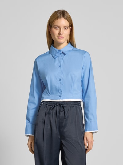 Frauenmodel trägt Cropped Hemdbluse mit gelegten Falten Modell 'Zopy' von Gestuz in Hellblau, aus elastischem Baumwoll-Mix, Hemdblusenkragen, langärmelig, durchgehende Knopfleiste, Rückenlänge 47 cm, Ärmellänge 63 cm, dezente Struktur, Ganzkörperansicht von vorne.