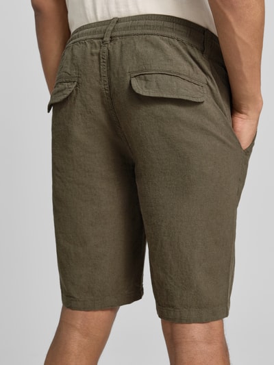 Männermodel trägt Bermudas aus Leinen-Mix mit französischen Eingrifftaschen von Lindbergh in Olive, Struktur sichtbar, Ganzkörperansicht Rückansicht, Herren, Leinen-Baumwoll-Mix, Straight Fit, Elastischer Bund mit Kordelzug, Knopf- und Reißverschluss, Gesäßtaschen, Bundweite bei Größe M: 43 cm, Innenbeinlänge bei Größe M: 24 cm.