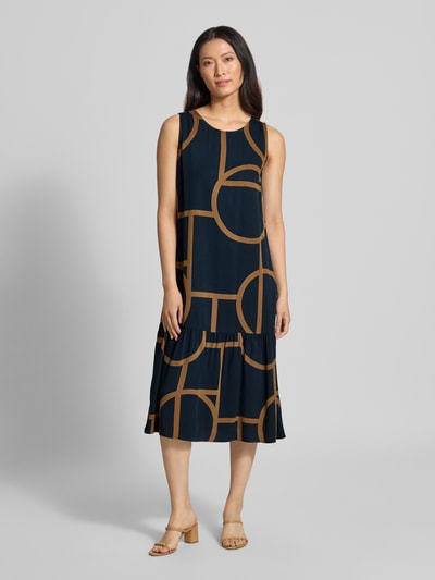 Modelka kobieca ma na sobie Ausgestelltes Freizeitkleid aus reiner Viskose Modell 'Wicy atelier' od OPUS w granatowym kolorze z dużym brązowym geometrycznym wzorem, tkanina gładka, sukienki casualowe; widok całej sylwetki z przodu.