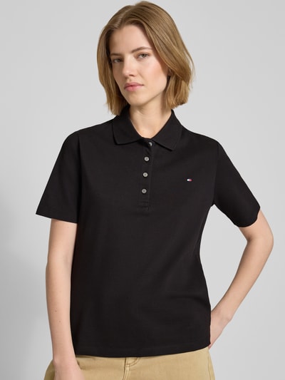 Frauenmodel trägt Regular Fit Poloshirts aus Baumwoll-Mix von Tommy Hilfiger, unifarben schwarz, kurzarm, V-Ausschnitt, Ganzkörperansicht von vorne.