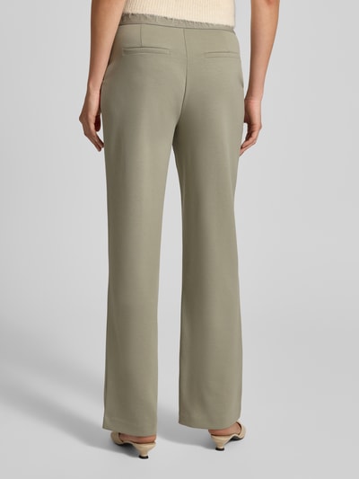 Frauenmodel trägt Stoffhose mit elastischem Logo-Bund von monari in Hellbeige, lockerer Schnitt, französische Eingrifftaschen, Ganzkörperansicht Rückansicht.