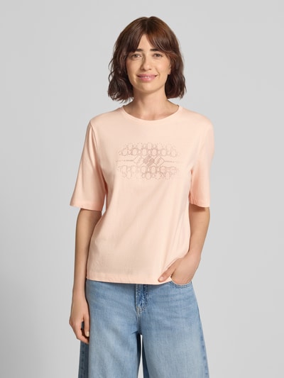 Frauenmodel trägt T-Shirt mit Ziersteinbesatz und Rundhalsausschnitt von Marc Cain, reine Baumwolle, Regular Fit, hellrosa Farbe, Ganzkörperansicht von vorne.
