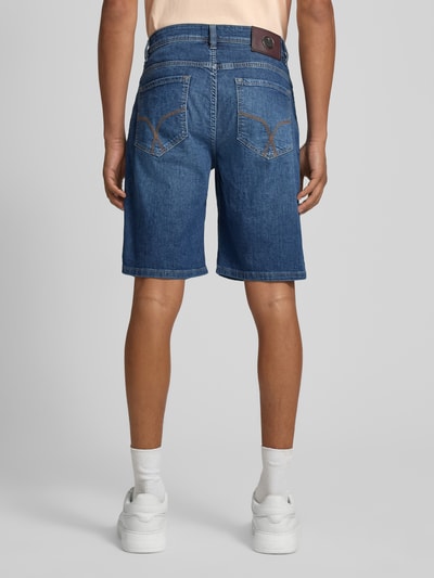 Męski model nosi bermudy w 5 kieszeni model 'Fort' od JOOP! kolekcja, mieszanka bawełny z dodatkiem streczu, krój straight fit, niebieski denim, detal: zapięcie na guzik i zamek błyskawiczny, szerokość w rozmiarze 32: 48 cm, długość wewnętrzna nogawki: 25 cm. Ganzkörperansicht Rückansicht.