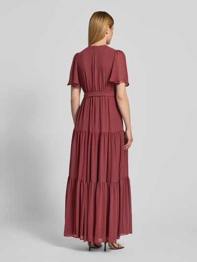 Frauenmodel trägt Abendkleid mit V-Ausschnitt und Bindegürtel von Christian Berg Cocktail aus Chiffon, Stufen-Look, A-Linie, Maxikleid, Rückenlänge bei Größe 36: 151 cm, Brustweite 41 cm, Ärmellänge 30 cm, Ganzkörperansicht Rückansicht.