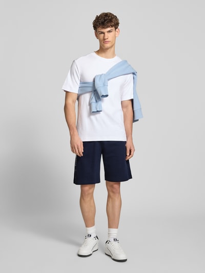 Männermodel trägt Shorts mit Logo-Print und -Stitching von CHAMPION in Dunkelblau, lockerer Schnitt, Baumwoll-Mix, Ganzkörperansicht von vorne.