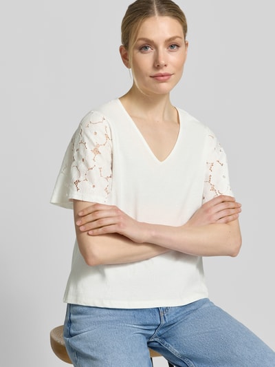 Frauenmodel trägt Regular Fit Blusenshirt aus reiner Baumwolle Modell 'VILLA' von Vero Moda, Optik: Unifarben, Spitzenbesatz, V-Ausschnitt, Kurzarm, Materialverarbeitung: Jersey, cremefarben, glatte Textur, Ganzkörperansicht von vorne.