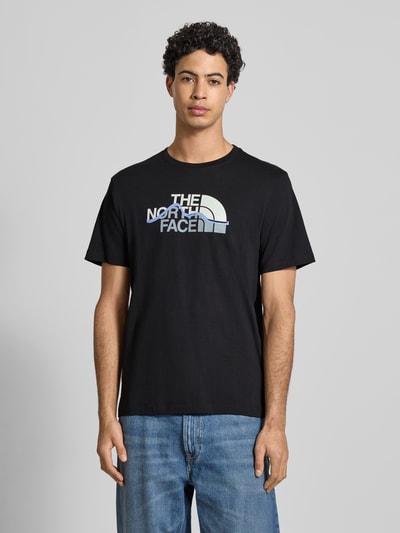 Mannenmodel draagt zwart Regular fit T-shirt uit puur katoen Model 'MOUNTAIN LINE' van The North Face met labelprint, ronde hals, ruglengte bij maat M 70 cm. Ganzkörperansicht von voren.