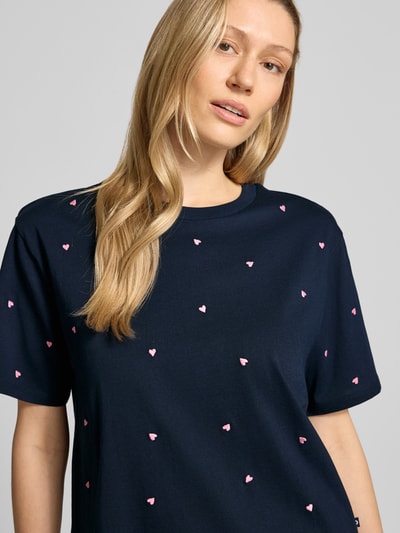 Frauenmodel trägt Boxy Fit T-Shirt aus reiner Baumwolle von Tom Tailor Denim in Dunkelblau mit rosa Herz-Stickerei, Nahaufnahme Oberkörper.