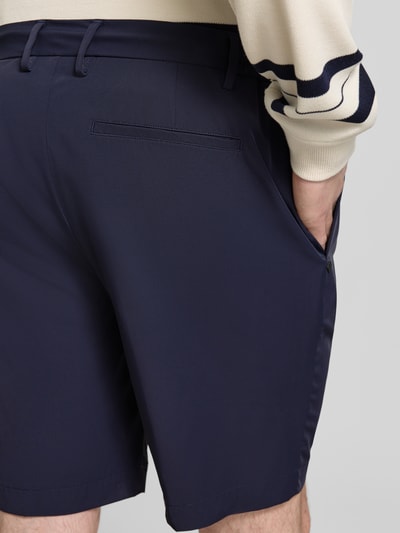 Männermodel trägt Pantalaccio Fit Bermudas mit Eingrifftaschen von MARKUP, Material-Mix mit Stretch-Anteil, dunkle Farbe, Detailaufnahme Rückansicht.