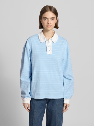 Frauenmodel trägt Relaxed Fit Poloshirt mit Label-Stitching Modell 'Jolina' von OH APRIL aus reiner Baumwolle in Hellblau mit weißem Spitzenbesatz und Knopfleiste, Rückenlänge bei Größe S 65 cm, Ganzkörperansicht von vorne.