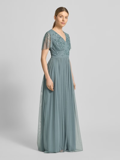 Modelka nosi sukienkę wieczorową 'Abendkleid mit Ziersteinbesatz' od Christian Berg Cocktail w kolorze niebieskim, linia a, długa sukienka, dekolt w serek, marszczenia, zamek błyskawiczny na plecach, obszycie ozdobnymi kamieniami, długość tyłu w rozmiarze 36: 140 cm, szerokość w rozmiarze 36: 38 cm, długość rękawów w rozmiarze 36: 21 cm. Pełny widok z przodu.
