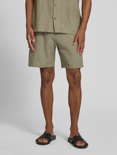 Männermodel trägt Shorts mit Strukturmuster Modell 'BILL' von Jack & Jones Premium in Olive, Straight Fit, Nahaufnahme Oberschenkel, Vorderansicht. Baumwoll-Mix mit Stretch, elastischer Bund mit Knopf, seitliche Eingrifftaschen, Gesäßleistentaschen.