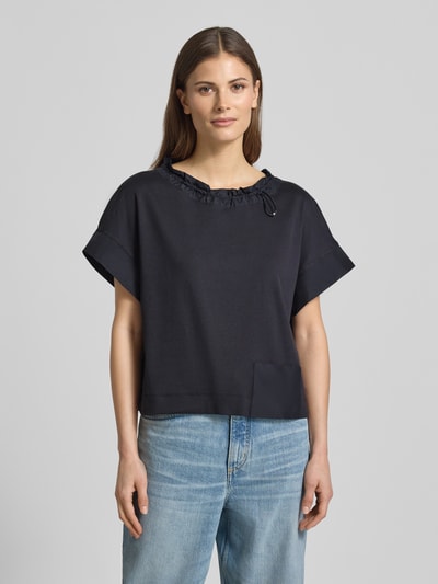 Kobiece model prezentuje t-shirt z wpuszczaną kieszenią przy dolnym brzegu od Marc Cain, mieszanka bawełny i elastanu, luźny krój, okrągły dekolt z tunelem, pas z tunelem, długość tyłu w rozmiarze 36: 51 cm, widok całej sylwetki z przodu.