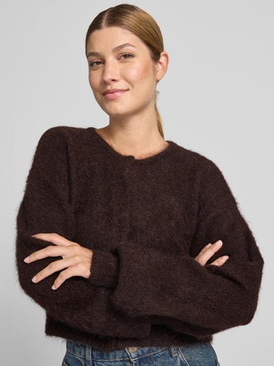 Modelka nosi Cropped kardigan rozpinany z mieszanki moheru i bawełny Model 'debbie' od Gestuz, okrągły dekolt, listwa guzikowa, kolor ciemnobrązowy, tekstura puszysta, widoczne niebieskie spodnie, długość tyłu 46 cm, długość rękawów 74 cm, widok z przodu, zbliżenie na górną część ciała.