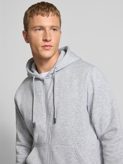 Männermodel trägt Sweatjacke mit Kapuze Modell 'BRADLEY' von Jack & Jones im Material-Mix mit Baumwoll-Anteil, lockere Passform, Reißverschluss, Kängurutasche, hellgrau-melierte Optik, Nahaufnahme Oberkörper.